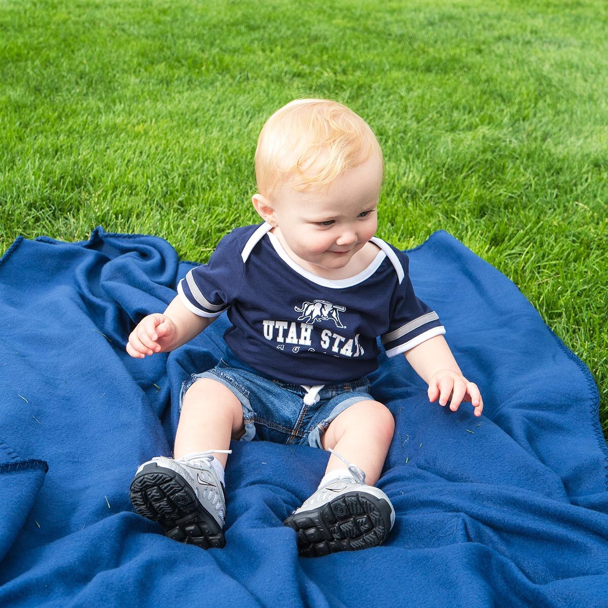 toddler boy wearing utah state aggies onesie sitting on blanket on the quad